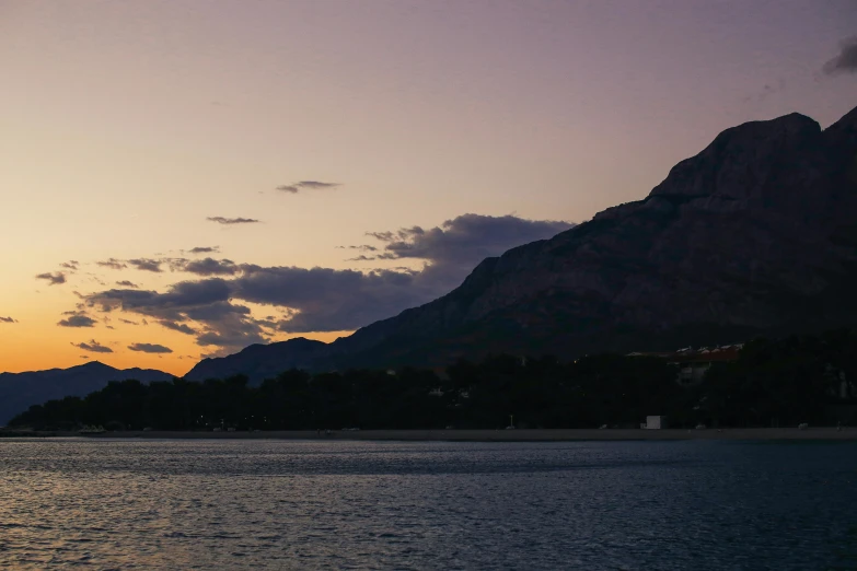 a large body of water with a mountain in the background, by Alexis Grimou, unsplash contest winner, romanticism, late evening, boka, slightly tanned, purple sky