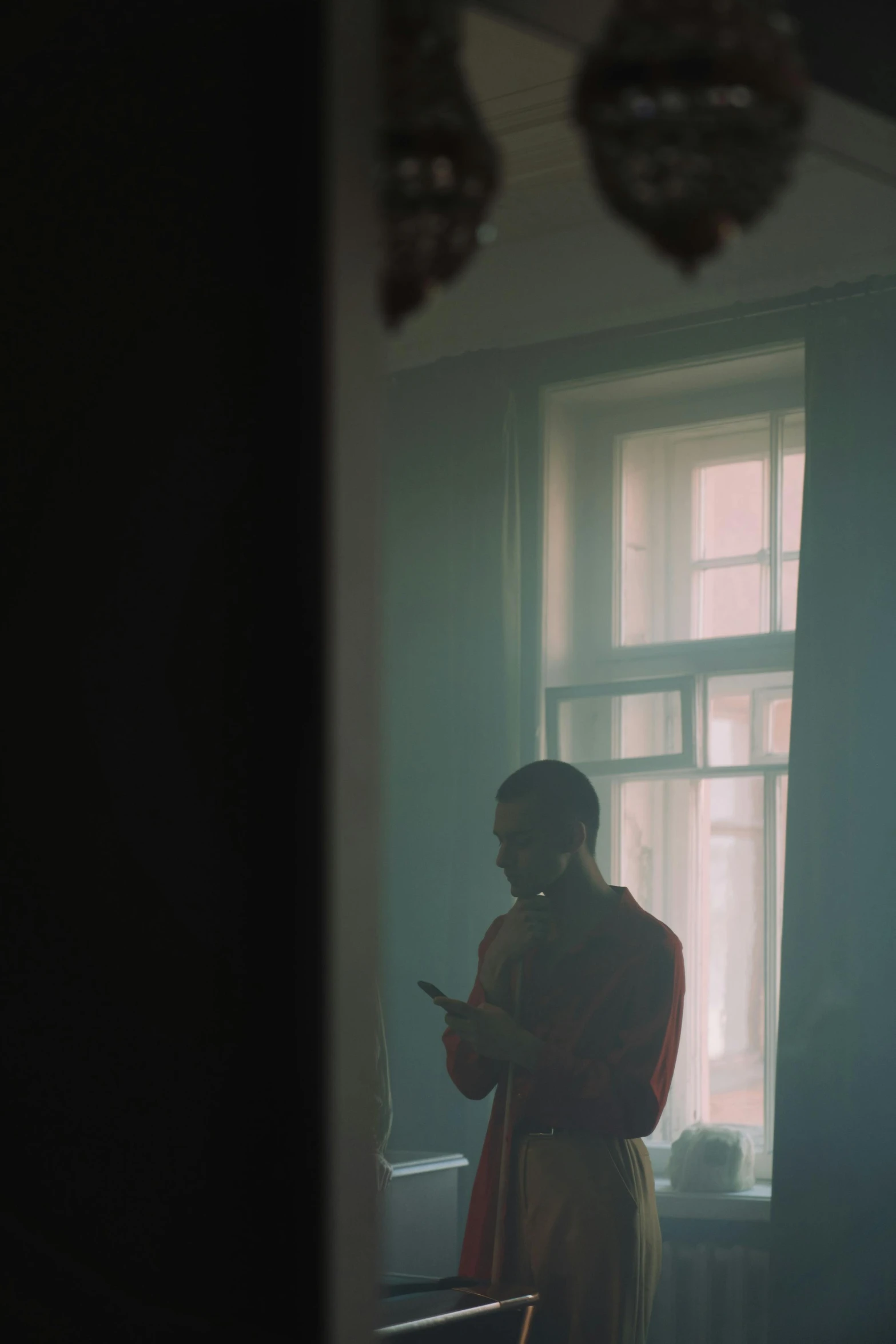 a woman standing in front of a window talking on a cell phone, a picture, inspired by Elsa Bleda, andrey tarkovsky, low quality photo, a young man, with red haze