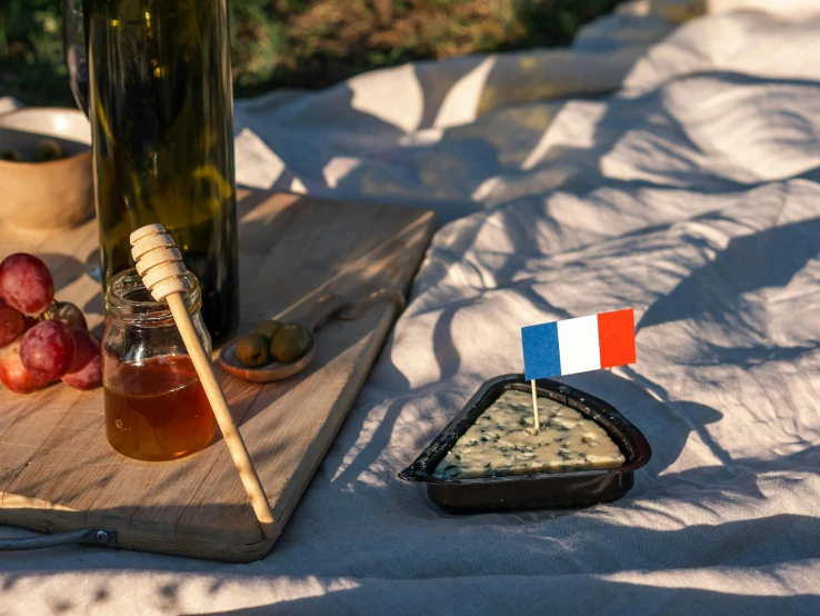 a bottle of wine sitting on top of a wooden cutting board, by Romain brook, figuration libre, flags, picnic, black, olive