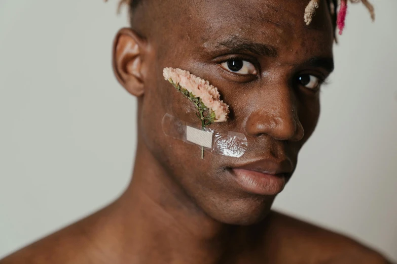 a man with a piece of tape on his face, trending on pexels, hyperrealism, with brown skin, flowers on heir cheeks, androgynous male, clean face and body skin