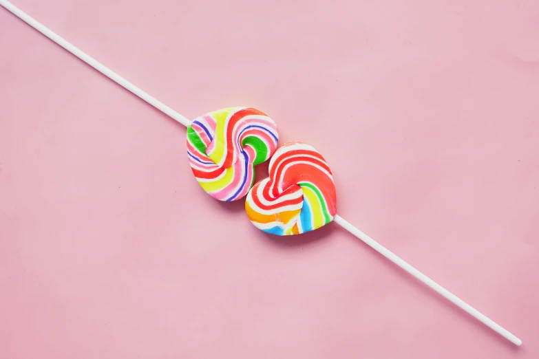 two lollipops on a stick against a pink background, inspired by Ödön Márffy, trending on pexels, pop art, swirly vibrant color lines, polymer clay, hairband, close up details