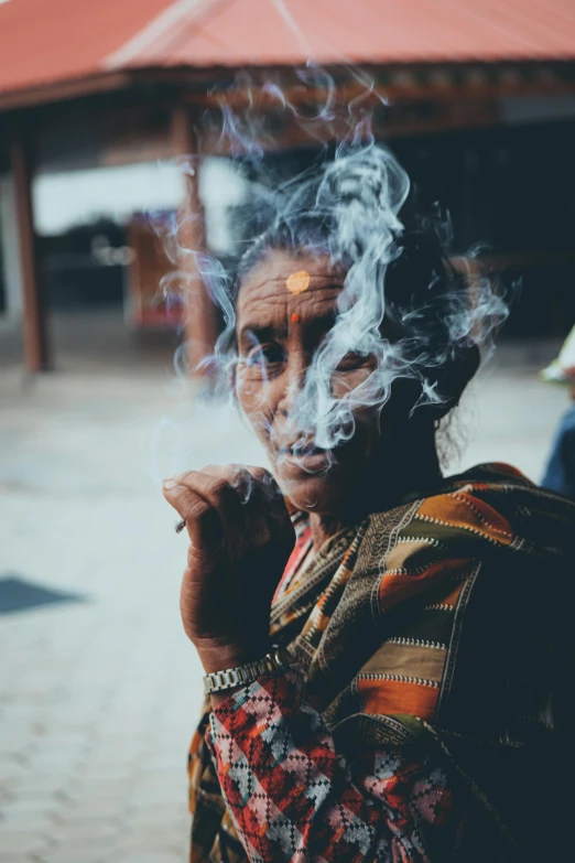 a woman smoking a cigarette in front of a building, an album cover, pexels contest winner, sumatraism, india tika third eye, marijuana smoke, old lady, haze over the shoulder shot