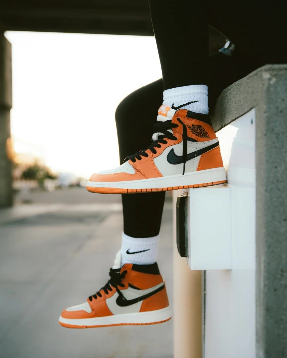 a person sitting on a ledge with their shoes on, an album cover, inspired by Jordan Grimmer, trending on pexels, orange and white color scheme, air jordan 1 high, thumbnail, light tan