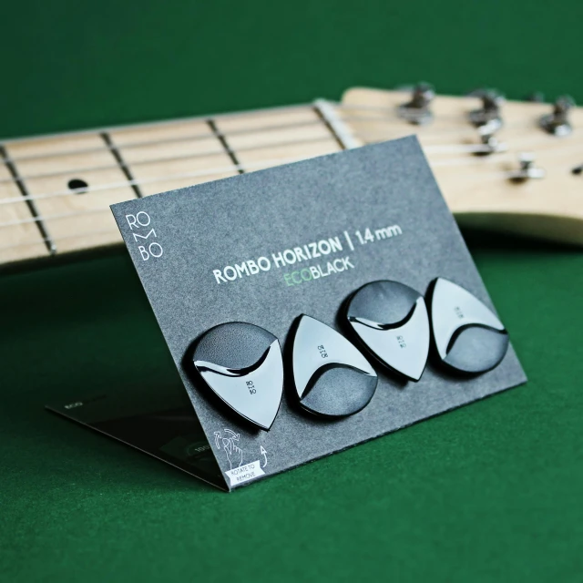 a business card sitting on top of a guitar, metallic buttons, all black matte product, three bat head, product photograph