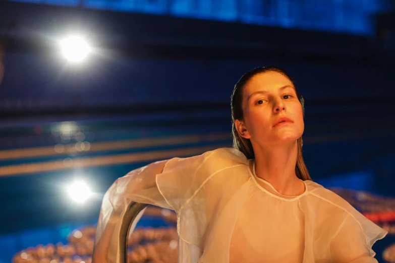 a woman in a white dress sitting at a table, a portrait, by Liza Donnelly, unsplash, bauhaus, futuristic fashion show, lit from below, sweating, cinema still