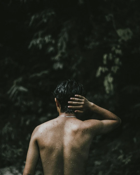 a man standing in the water with his back to the camera, an album cover, trending on unsplash, sumatraism, non binary model, ((forest)), bare shoulders, with a black background