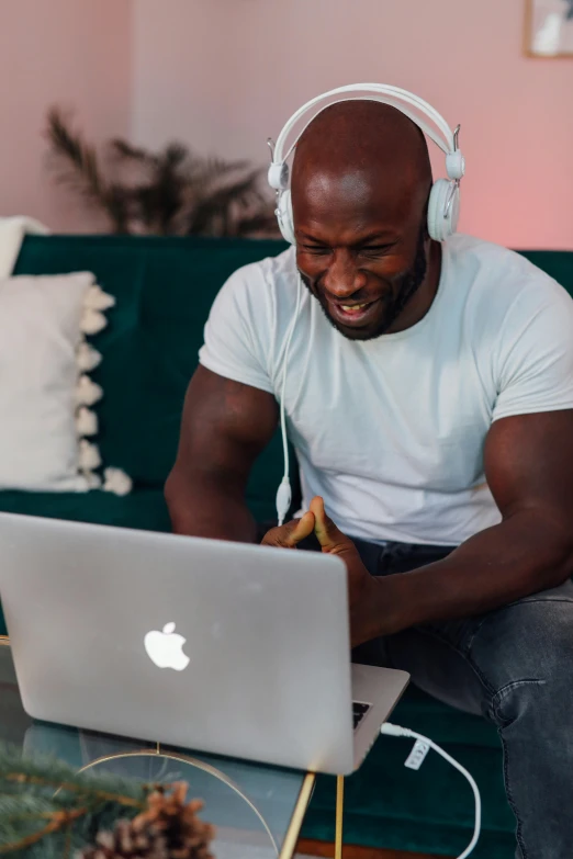 a man sitting on a couch using a laptop, an album cover, inspired by Michael Gustavius Payne, pexels contest winner, happening, african man, pink headphones, muscular bald man, profile image