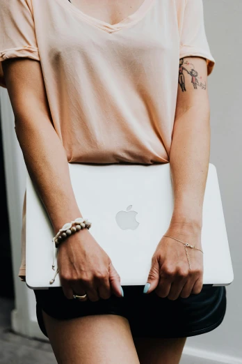 a woman holding a laptop computer in her hands, by Carey Morris, trending on pexels, renaissance, photograph of a sleeve tattoo, apple logo, wearing two silver bracelets, wearing a light shirt