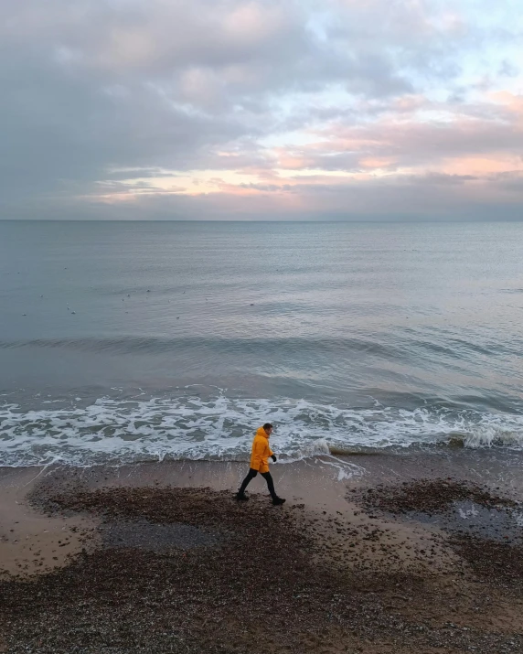 a person walking on a beach near the ocean, standing next to water, wearing a yellow hoodie, photo of the middle of the ocean, ignant
