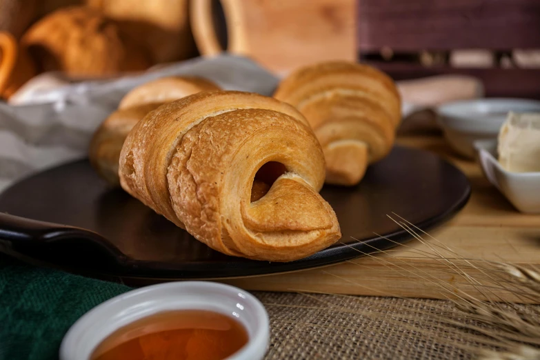 a plate that has some croissants on it, inspired by Károly Patkó, unsplash, photorealism, on a wooden tray, twinkling and spiral nubela, close-up product photo, high quality product image”