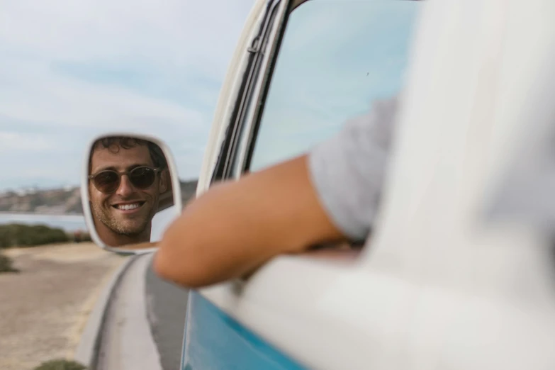 a man taking a picture of himself in the side mirror of a van, by Lee Loughridge, pexels contest winner, smiling male, kombi, thumbnail, ultrawide image