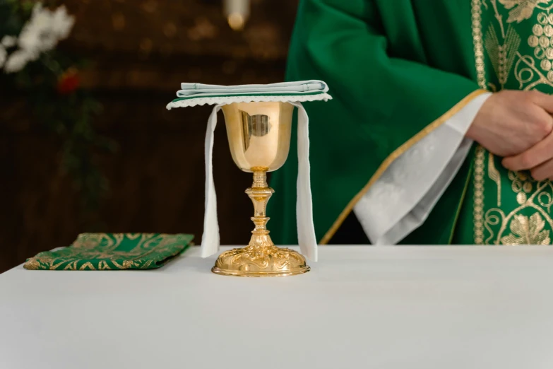 a priest holding a cross in front of a chalicet, by Joseph Severn, trending on unsplash, overturned chalice, gold and green, gold cloth, marsterpiece