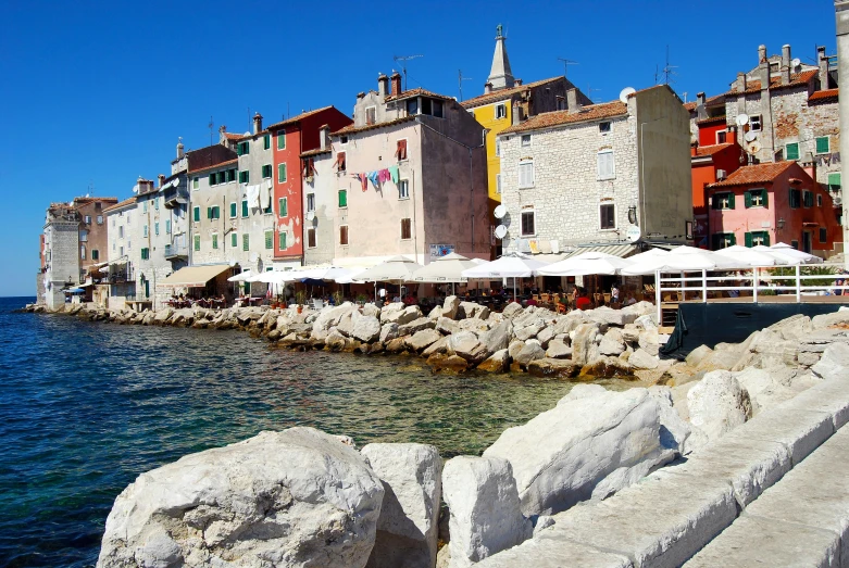 a group of buildings sitting next to a body of water, a photo, croatian coastline, al fresco, rocky beach, exterior photo