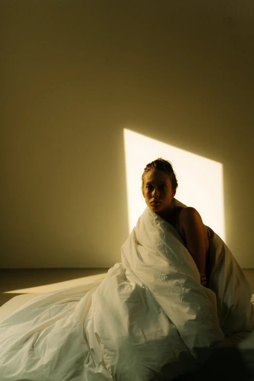 a woman sitting on top of a bed covered in a blanket, light and space, white cloth in wind shining, promo photo, ignant, sun lit