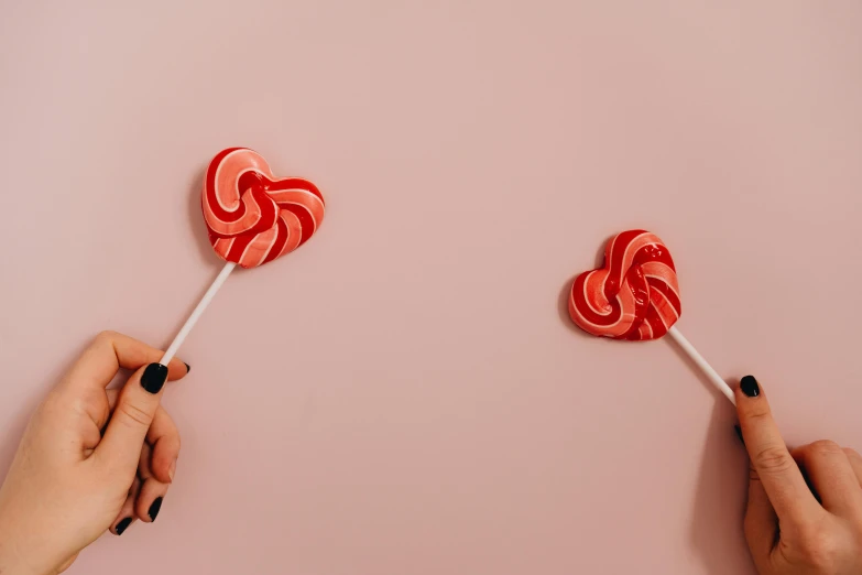 two hands holding two lollipops on a pink surface, trending on pexels, background image, red swirls, instagram photo, profile photo