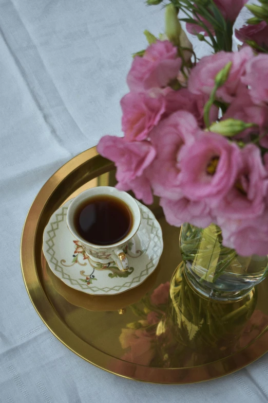 a vase filled with pink flowers next to a cup of coffee, inspired by Eugène Isabey, moroccan tea set, golden, medium close shot, linen