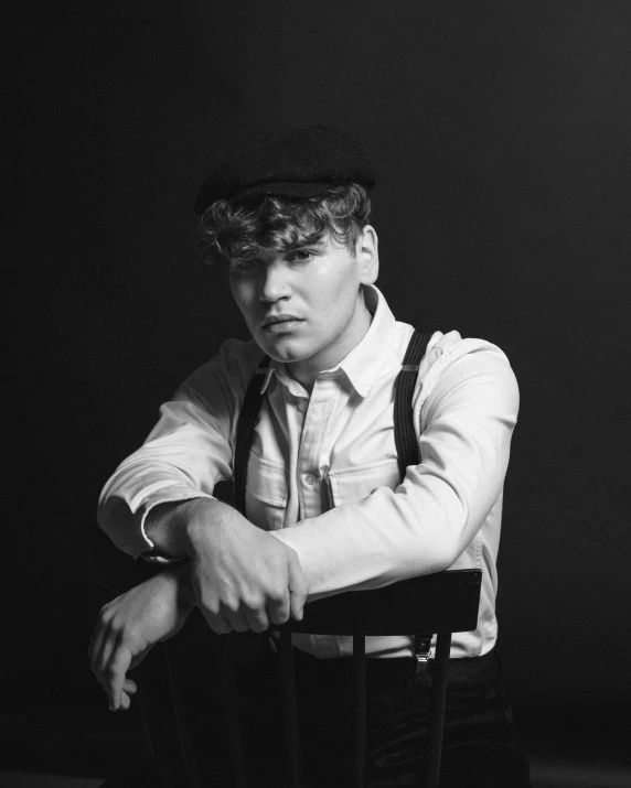 a black and white photo of a man sitting in a chair, inspired by August Sander, unsplash, costumes from peaky blinders, cute young man, ariel perez, suspenders