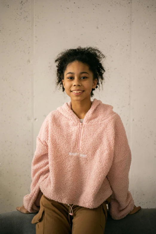 a young girl sitting on top of a couch, by Lily Delissa Joseph, trending on unsplash, wearing a pastel pink hoodie, portrait willow smith, confident pose, curly