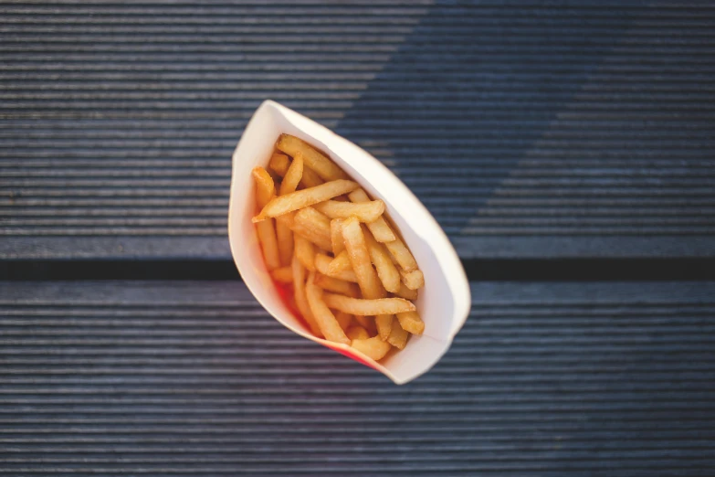 a paper container filled with french fries on top of a wooden table, inspired by Pia Fries, unsplash, breton cap, al fresco, dof narrow, frying nails