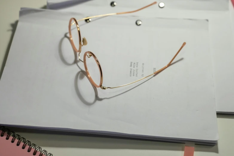 a pair of glasses sitting on top of a piece of paper, light pink tonalities, low quality photo, shot on sony a 7, gold wires