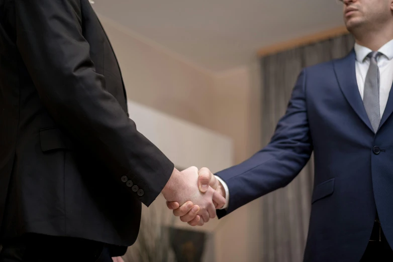 two men in suits shaking hands in a room, a picture, colour corrected, thumbnail, customers, suits