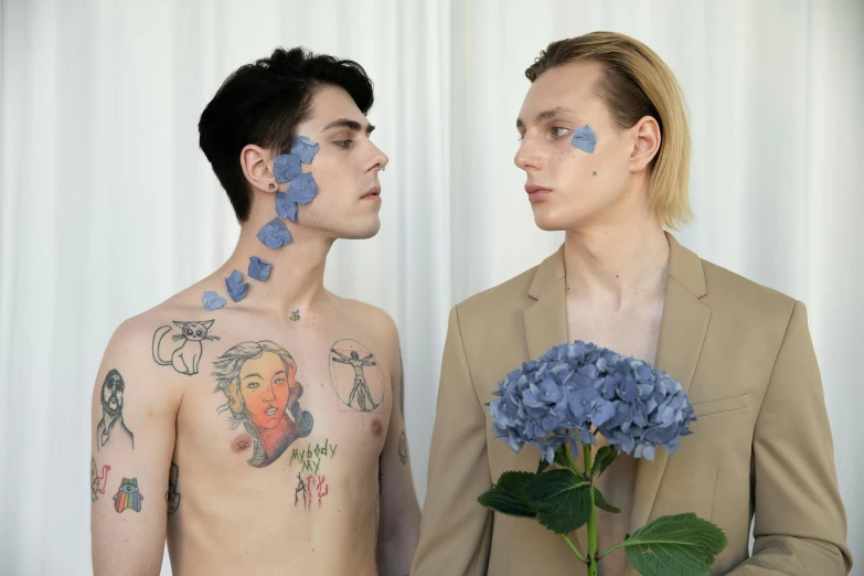 a couple of men standing next to each other, a tattoo, by Jessie Alexandra Dick, aestheticism, with blue skin, nonbinary model, flowers in background, margiela campaign