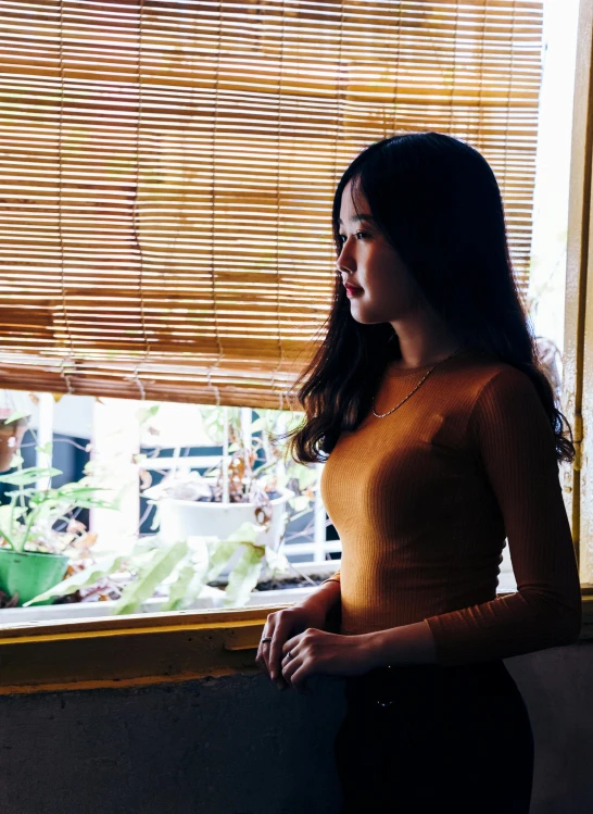 a woman standing in front of a window, inspired by Elsa Bleda, unsplash, realism, young asian girl, 🤤 girl portrait, yellow hue, panoramic view of girl