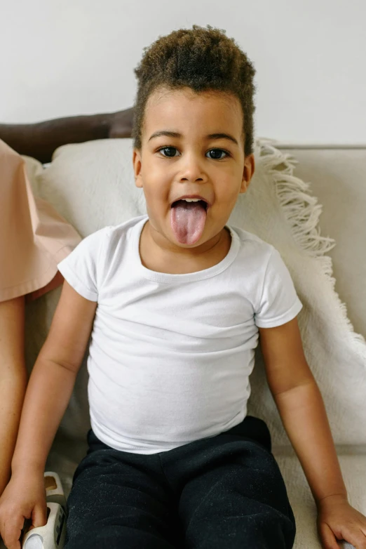 a little boy sitting on top of a couch next to a woman, long tongue, dressed in a white t shirt, mixed race, tummy