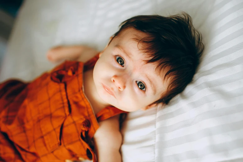 a close up of a child laying on a bed, pexels, hyperrealism, brown hair and large eyes, orange fluffy belly, caring fatherly wide forehead, adorably cute