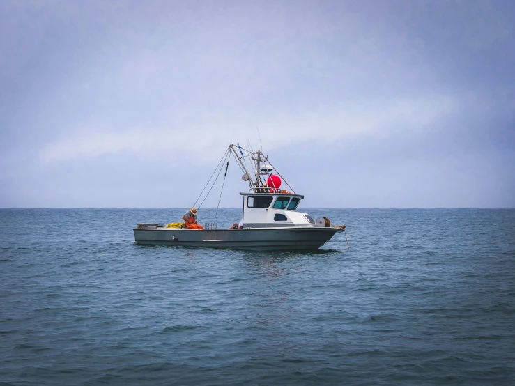 a boat in the middle of a body of water, wearing a fisher 🧥, at the sea, commercial photo, overcast day