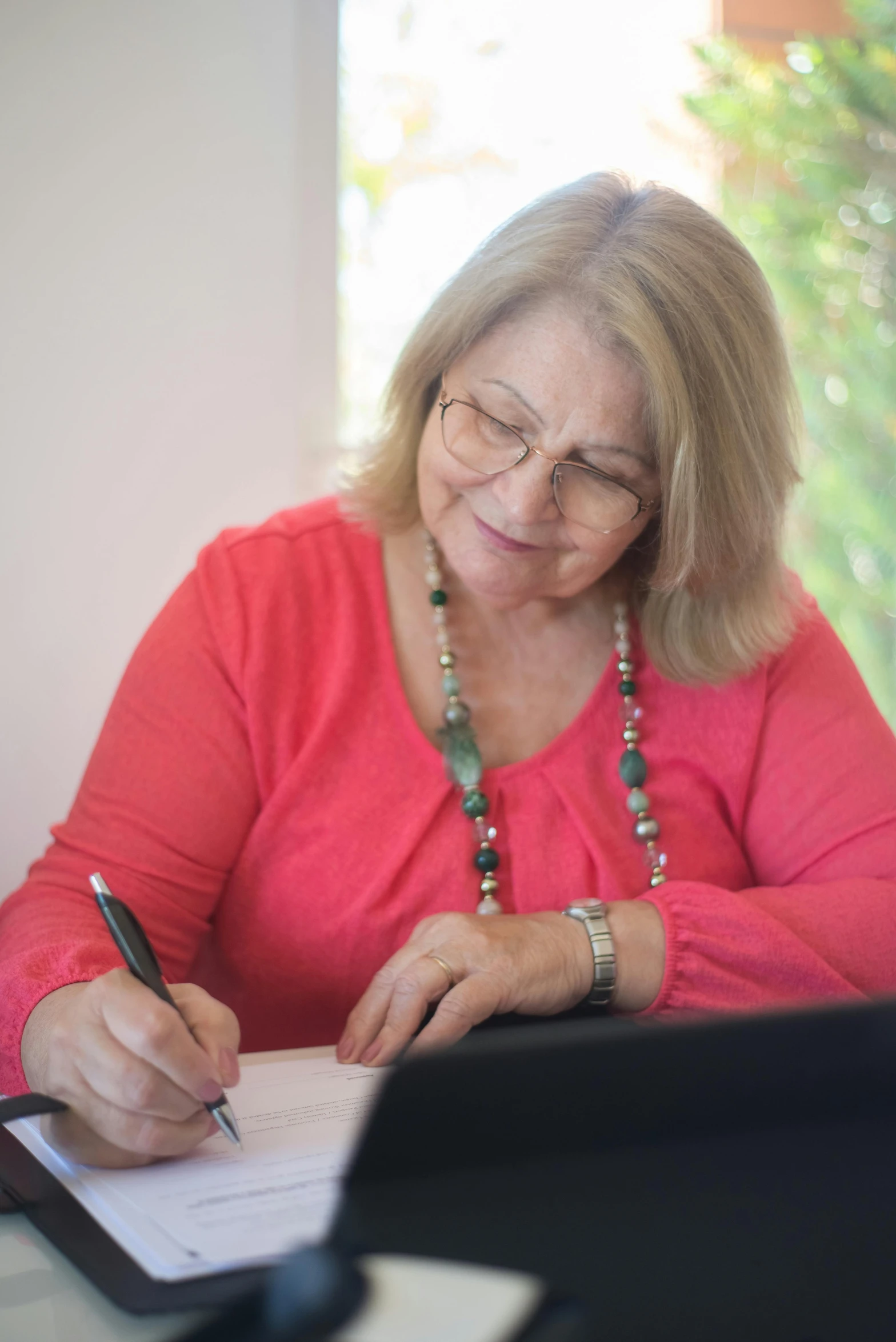 a woman sitting at a desk writing on a piece of paper, by Lynn Pauley, working on her laptop, older woman, high quality photo, multiple stories