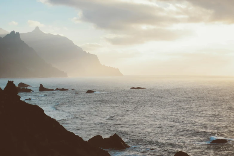 a person standing on top of a cliff next to the ocean, in a sunset haze, azores, unsplash photography, slide show