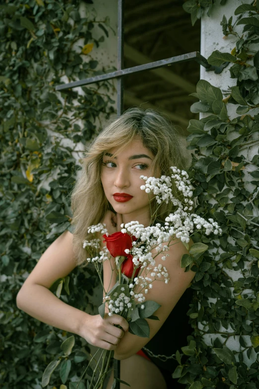 a woman holding a bouquet of flowers in front of a building, an album cover, inspired by Elsa Bleda, trending on pexels, red lipstick on face, imogen poots, flowers and vines, indoor picture