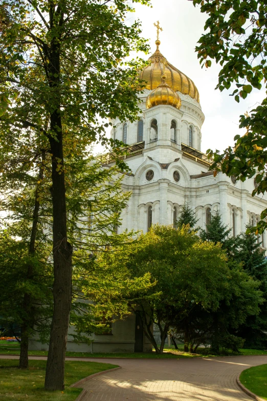 a large white building with a golden dome, inspired by Mikhail Lebedev, trees in background, gold and red, sanctuary, lush surroundings