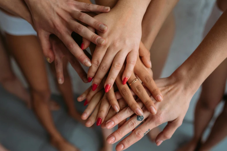 a group of people putting their hands together, a photo, trending on pexels, antipodeans, nail polish, woman holding another woman, piled around, wolfy nail
