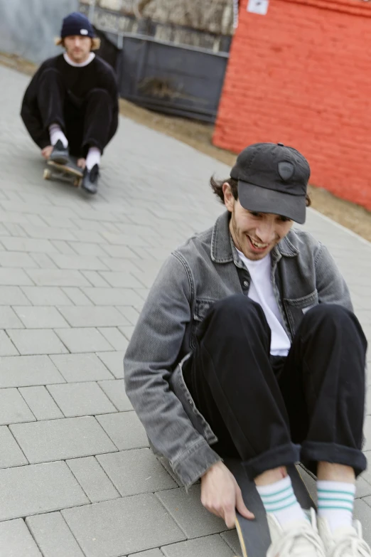 a couple of young men riding skateboards down a sidewalk, skin : tjalf sparnaay, sitting on the ground, baggy clothing and hat, soft cracks