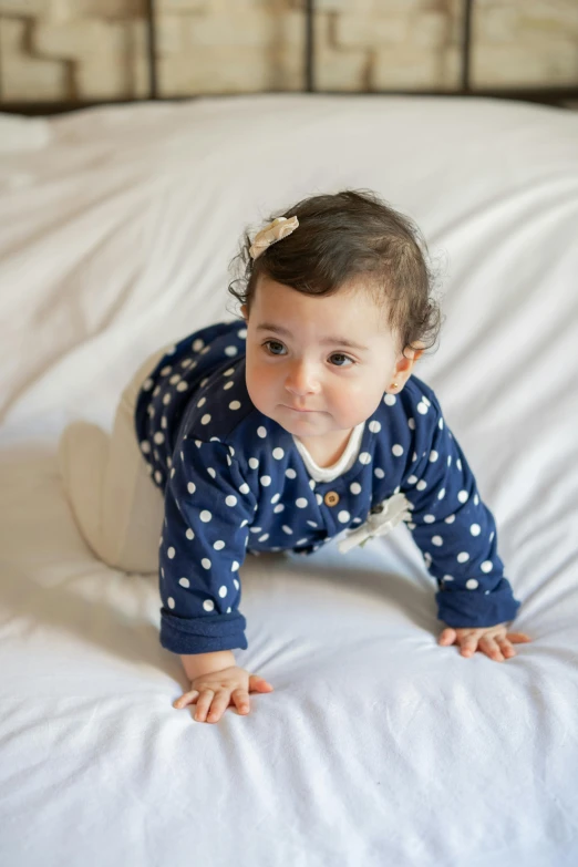 a little girl laying on top of a bed, navy, crawling towards the camera, varying dots, full product shot