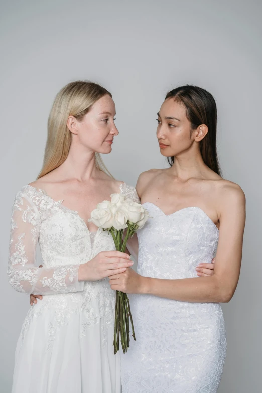 two women in wedding dresses standing next to each other, by Robbie Trevino, hand on cheek, product introduction photo, diverse, laura watson