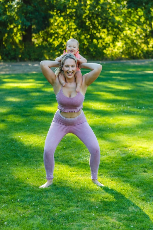 a woman holding a baby standing on top of a lush green field, two piece workout clothes, silly, a blond, abcdefghijklmnopqrstuvwxyz