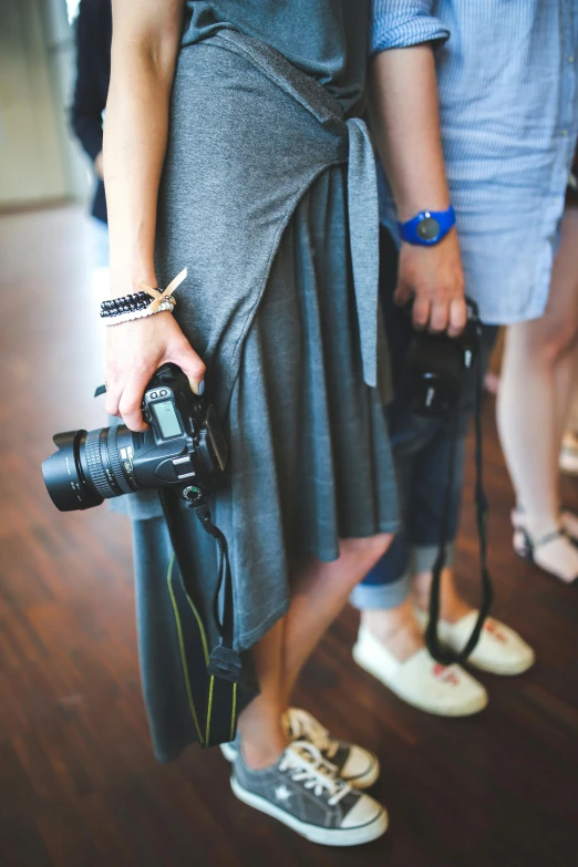 a woman in a gray dress holding a camera, unsplash, photorealism, event photography, holding arms on holsters, person in foreground, vacation photo