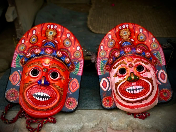 a couple of masks sitting on top of a table, inspired by Steve McCurry, pexels contest winner, bengal school of art, colorful with red hues, nepal, hindu god, welcoming grin
