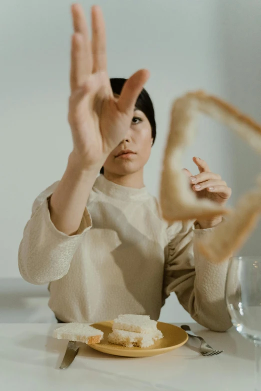 a woman sitting at a table with a plate of food in front of her, an album cover, inspired by Fei Danxu, unsplash, conceptual art, sliced bread in slots, gestures, in an action pose, oyasumi punpun