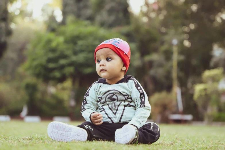 a baby sitting on top of a lush green field, pexels contest winner, streetwear, vinayak, beanie, at a park