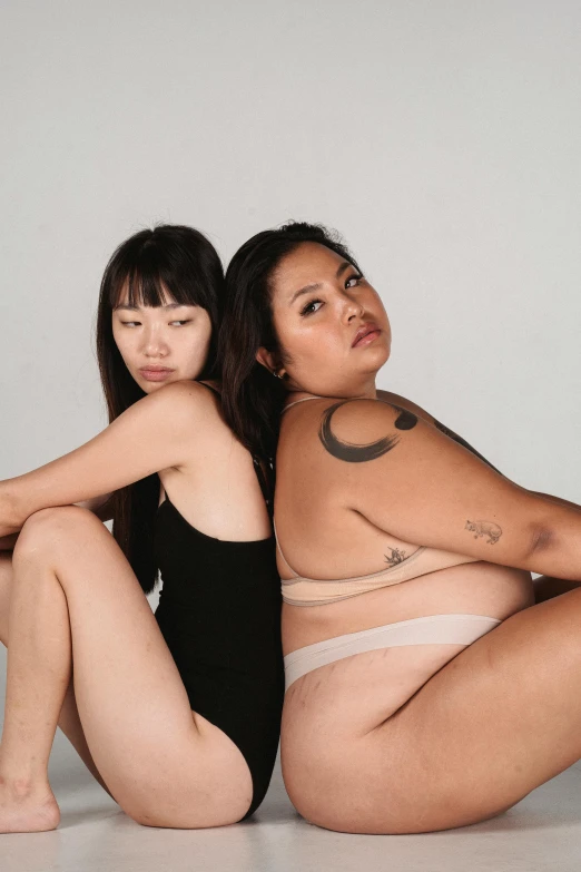 a couple of women sitting next to each other, inspired by Wang Duo, unsplash, realism, her belly is fat and round, half asian, bare thighs, nonbinary model