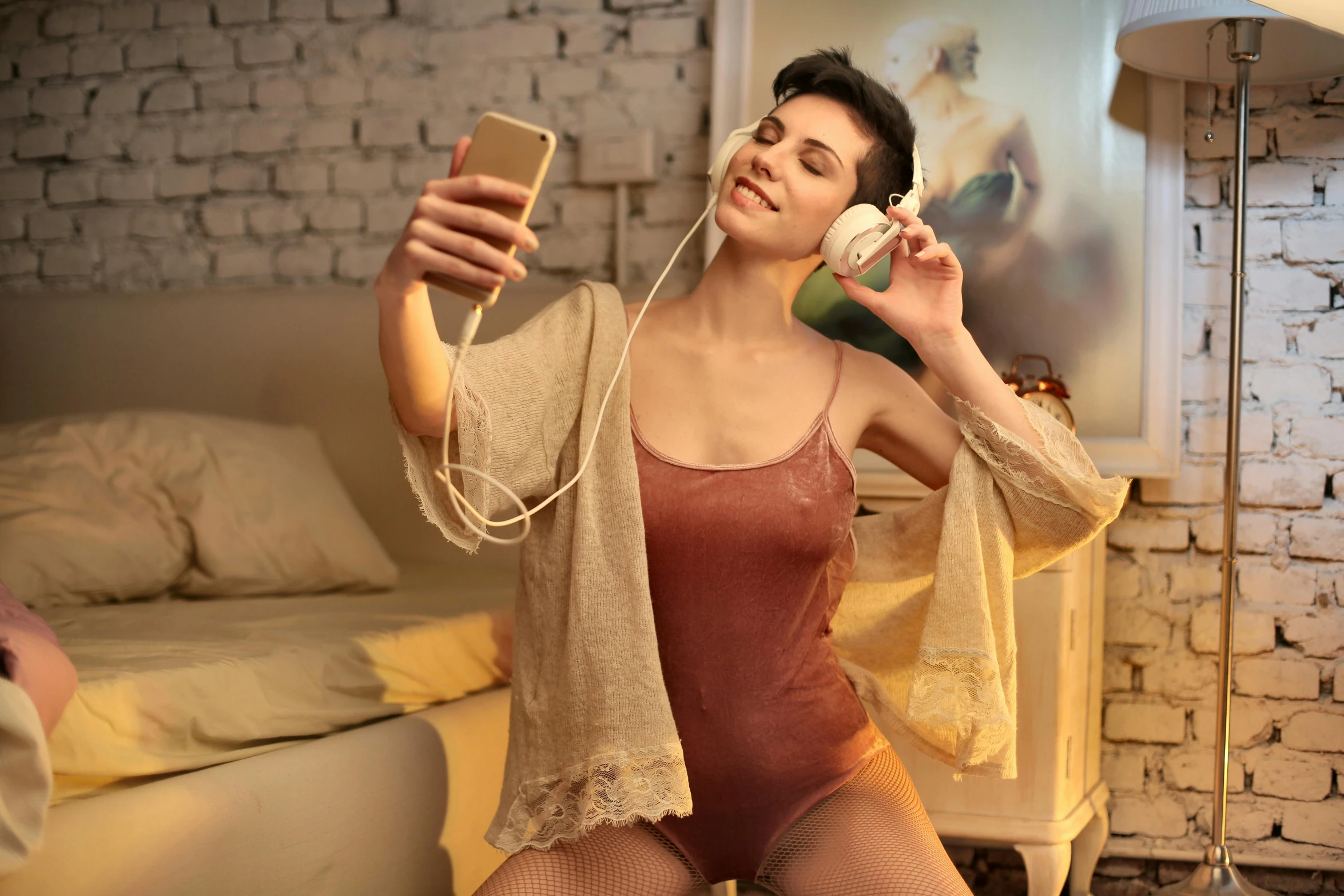 a woman sitting on a bed holding a cell phone, inspired by Hovsep Pushman, trending on pexels, fantastic realism, sensual dancing, with head phones, 8k selfie photograph, wearing leotard