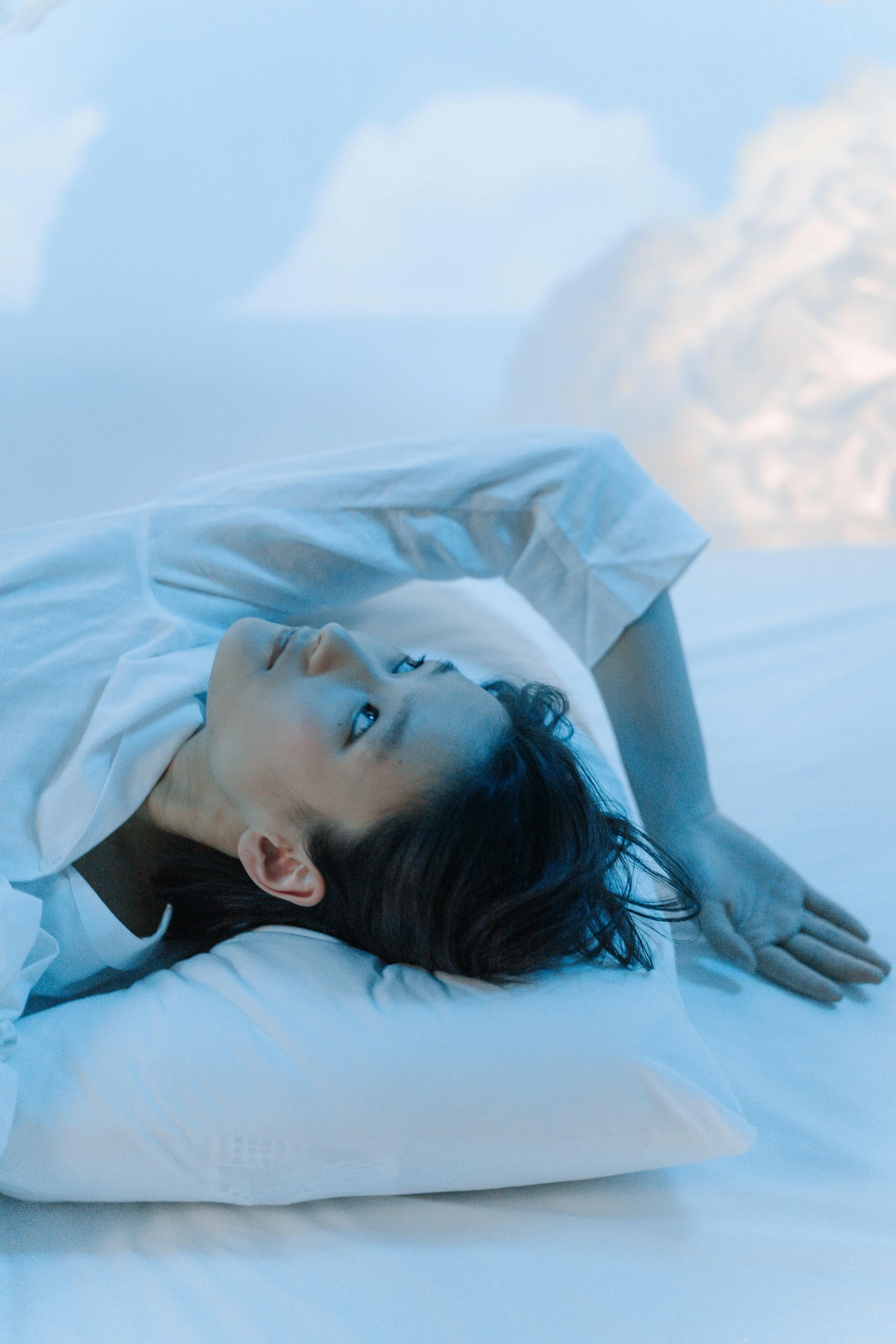 a woman laying on top of a pillow on a bed, inspired by Elsa Bleda, unsplash contest winner, conceptual art, teamlab, soft blue light, looking to the side, soft volumetric lighting