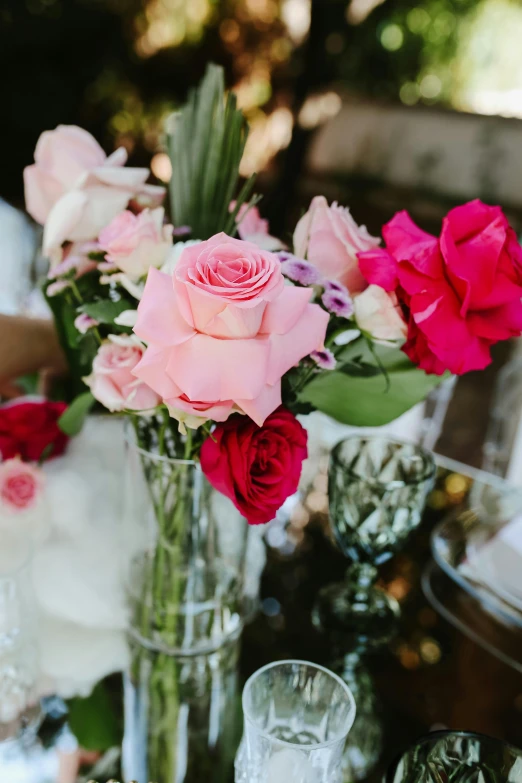 a close up of a vase of flowers on a table, pink accents, red roses, glassware, sophisticated composition