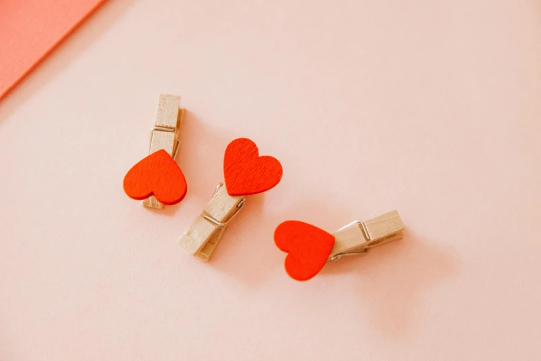 a couple of red hearts sitting on top of a pink surface, a picture, by Emma Andijewska, trending on pexels, tiny sticks, orange color, wooden, rule of three