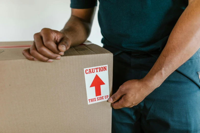 a man holding a box with a sticker on it, trending on pexels, orange safety labels, brown, redundancy, carson ellis