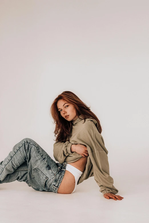 a woman sitting on the floor with her legs crossed, trending on pexels, photorealism, woman in streetwear, exposed midriff, white backdrop, green and brown clothes